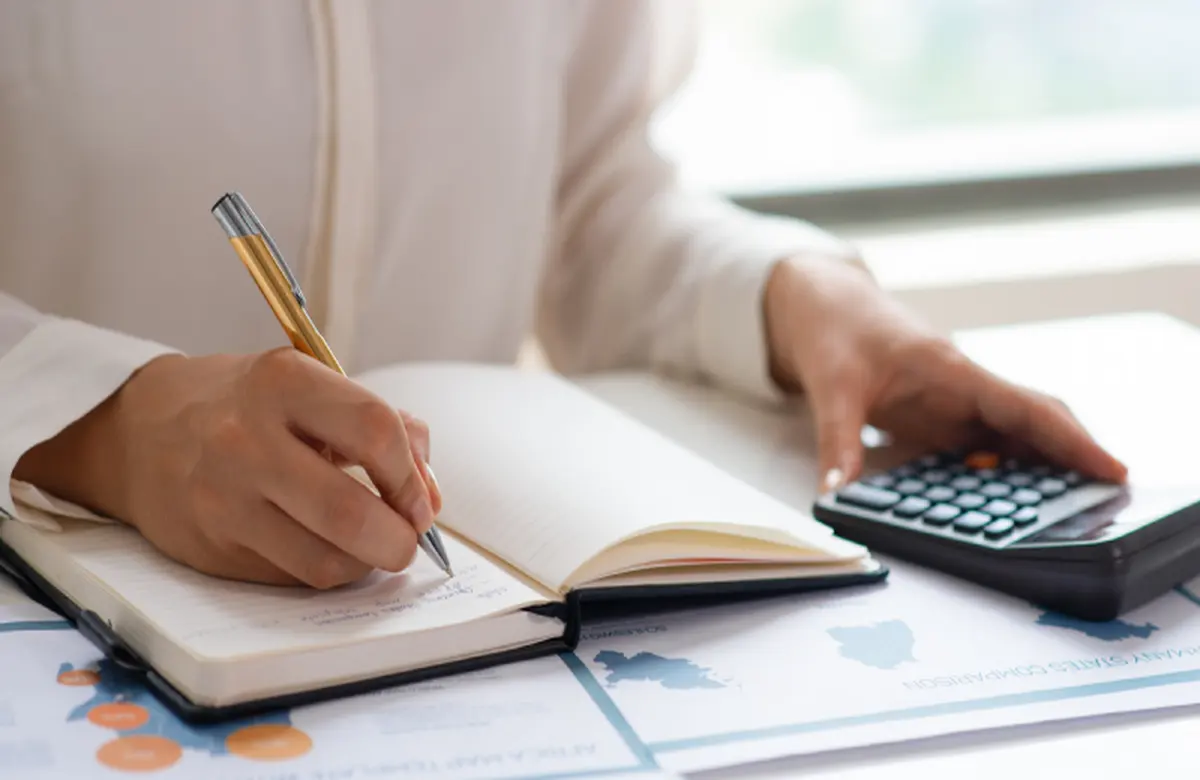 A work desk with an open notebook, a pen, a calculator, and printed charts.